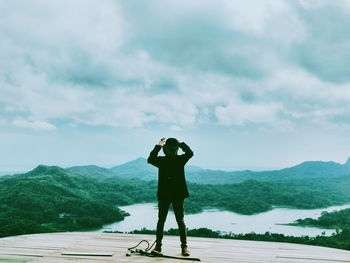 Rear view of man standing on mountain against sky