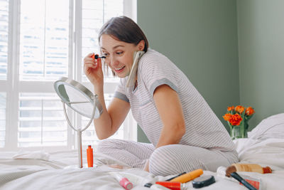 Woman doing make up while sitting on bed at home