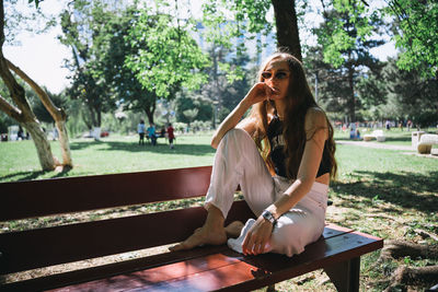 Portrait of young woman sitting on bench at park