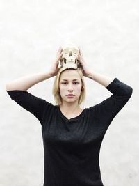 Portrait of young woman holding human skull against sky