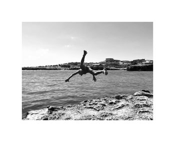 Men jumping on rock by sea against clear sky