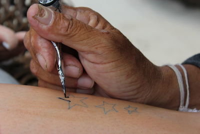 Cropped hand applying henna tattoo on person body