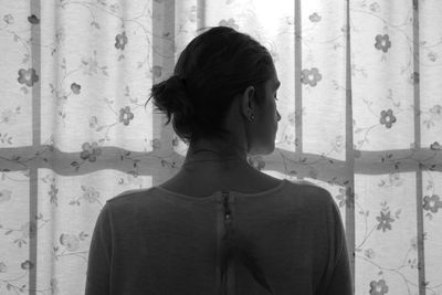 Rear view of woman with hair bun standing against curtain at home