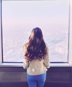 Rear view of woman looking at cityscape through window