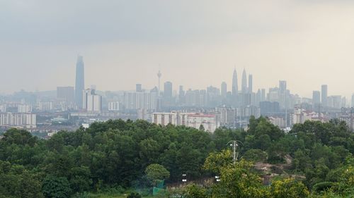 Trees and buildings in city against sky