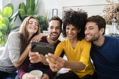 Four happy friends sitting on couch taking a selfie