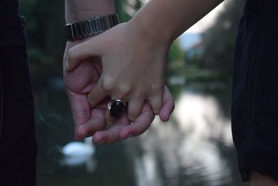 Cropped image of couple holding hands by lake