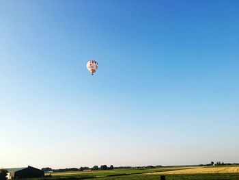 Hot air balloon flying over field against clear blue sky