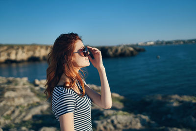 Young woman wearing sunglasses standing against sea