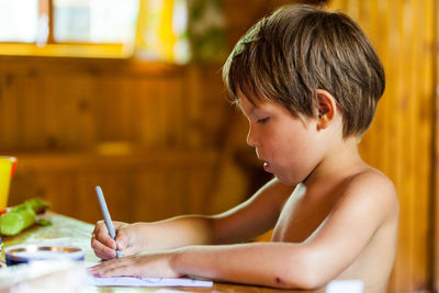 Side view of shirtless boy drawing at home