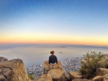 Rear view of woman sitting on cliff