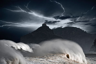 Scenic view of sea by mountain against sky