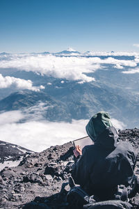 Man sitting on snowcapped mountain against sky