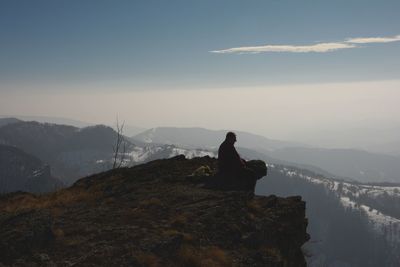 Man sitting on cliff against mountains