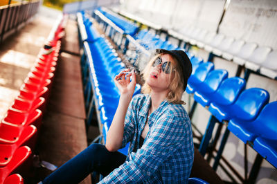 Young woman smoking cigarette on seat at stadium