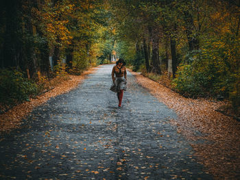 Full length of woman walking on footpath with fallen autumn leaves