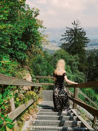 Rear view of woman standing on staircase against trees