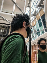 Low angle portrait of man standing by his mirrored reflection against architectural features