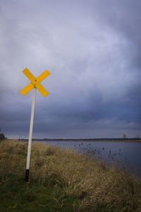 Road sign at grassy lakeshore against cloudy sky