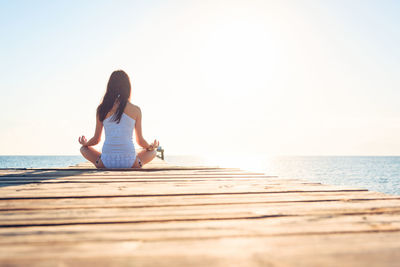 Full length of woman sitting on beach against clear sky