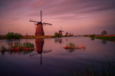 Traditional windmill by lake against sky during sunset