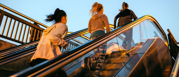 Women friends training running up escalator in city on sunset