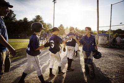 Baseball teams high fiving on field during sunset