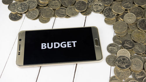 High angle view of budget text in smart phone by coins on table