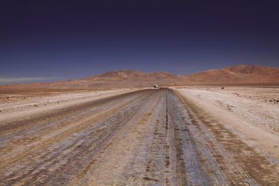 Road amidst desert against clear blue sky