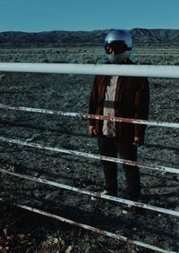 Man wearing crash helmet standing by railing on field