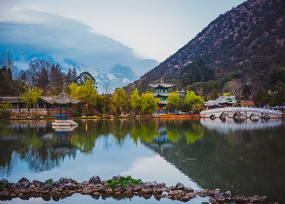 Scenic view of lake by trees and houses against sky