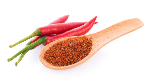 Close-up of red chili peppers and spoon on white background