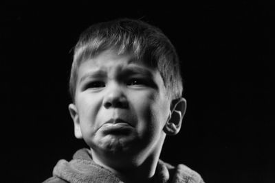 Close-up of cute boy looking away while crying against black background