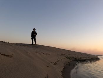 Full length of man standing on beach against sky during sunset