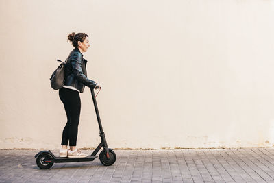 Side view of woman riding electric scooter wall
