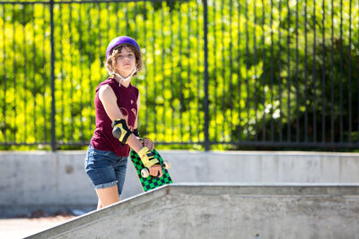 Skater girl holds her skateboard while looking toward the camera