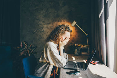 Side view of young woman using laptop while sitting at home