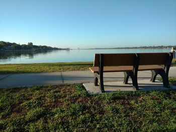 Bench in park by lake against clear sky