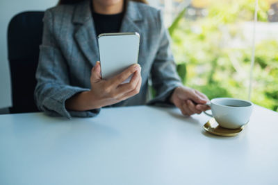 Midsection of woman using mobile phone while sitting on table