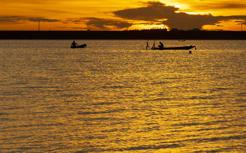 Silhouette people on sea against sky during sunset