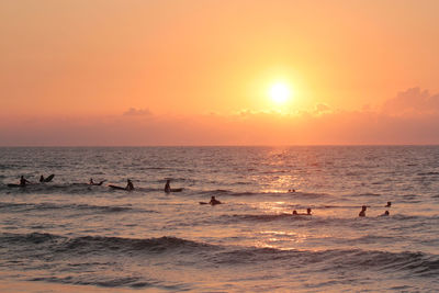 People surfing in sea against orange sky during sunset