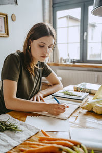 Young female food stylist writing in diary while working in studio