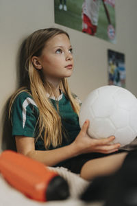 Elementary girl with soccer ball contemplating while sitting in bedroom