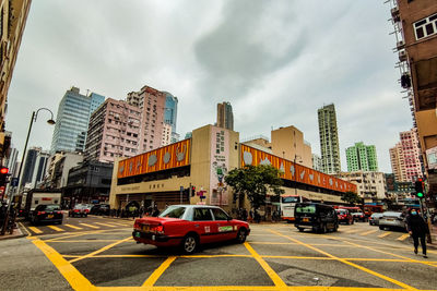 Cars on city street by buildings against sky