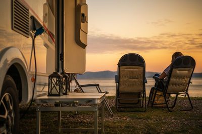 Mature woman sitting on chair by motor home during sunset