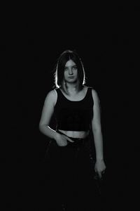 Portrait of young woman standing against black background