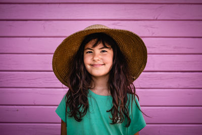 Portrait of smiling girl in straw hat against bright pink wall