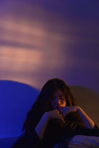 Side view of young woman sitting on beach against sky during sunset