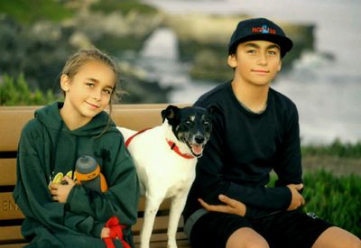 Portrait of siblings sitting with dog on bench