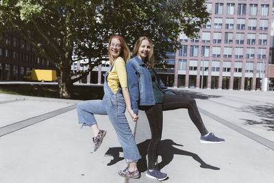 Playful young friends standing back to back on one leg